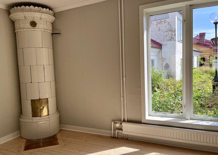 Kakelugn i lägenheten. Trädgården ut genom fönstret. Foto: Johan Jönsson